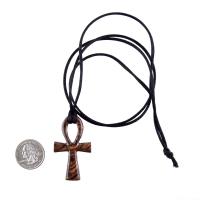 A wooden ankh pendant necklace with a black satin cord ending in a knot. The ankh is reddish-brown with a wood grain pattern.