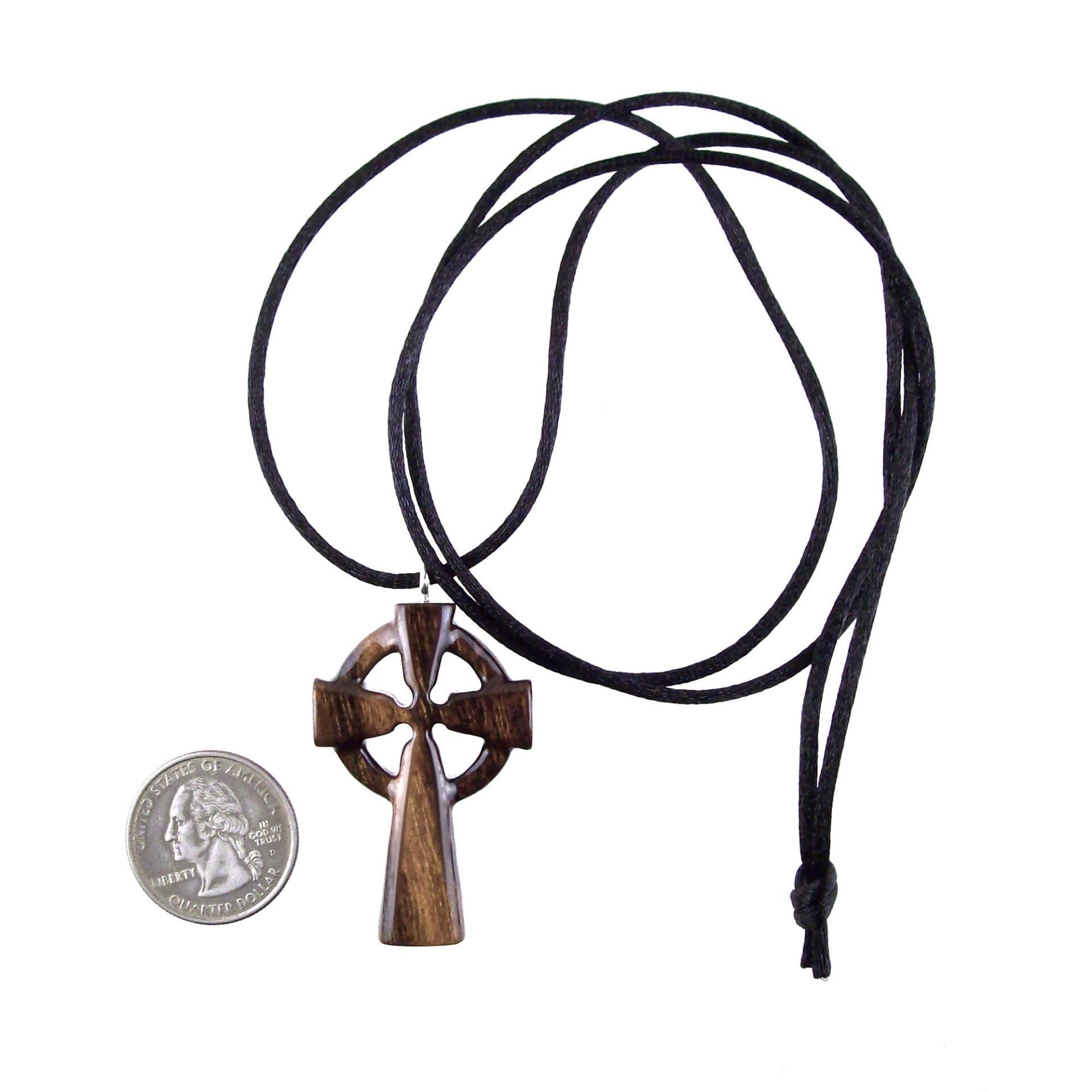 A brown wooden celtic cross pendant with black cord ending with a knot next to a US quarter to show scale. 